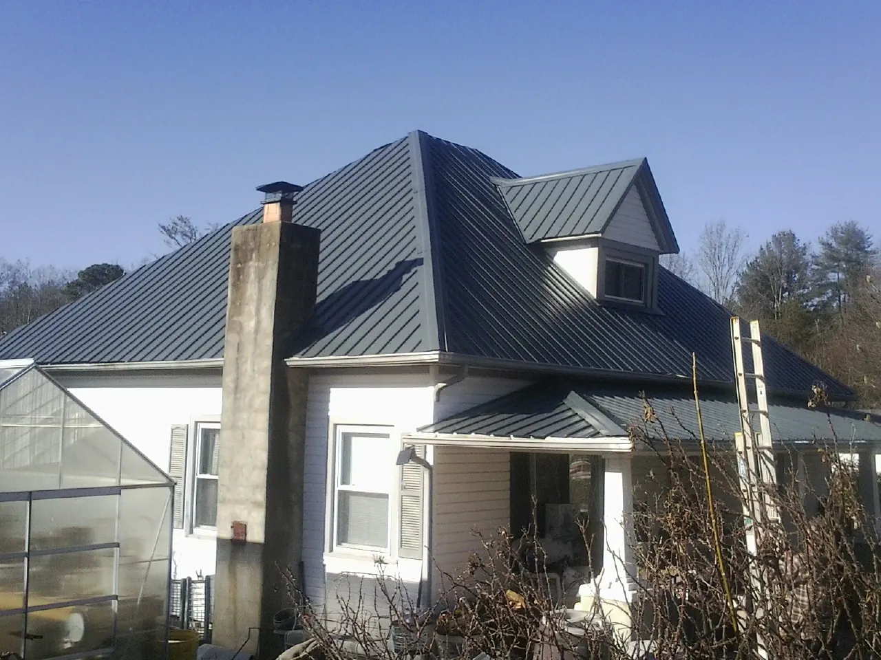 Dark blue standing seam metal roof on a white farmhouse with dormer — Slate & Tile Roof Repair by Roofing Brothers in Beaver Dams