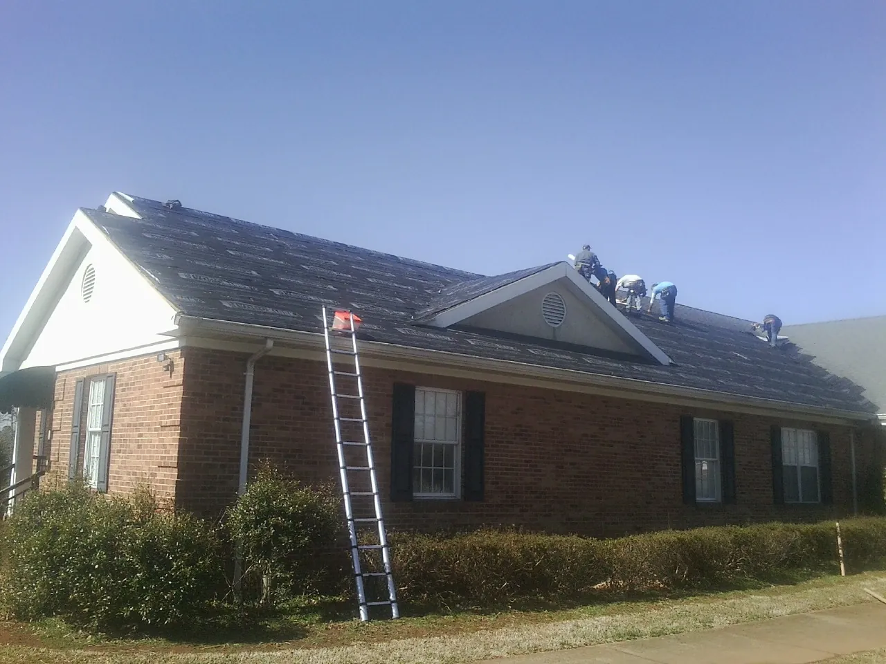 Crew tearing shingles off a brick ranch roof with a ladder set — Emergency Roof Repair work by our crew in Beaver Dams
