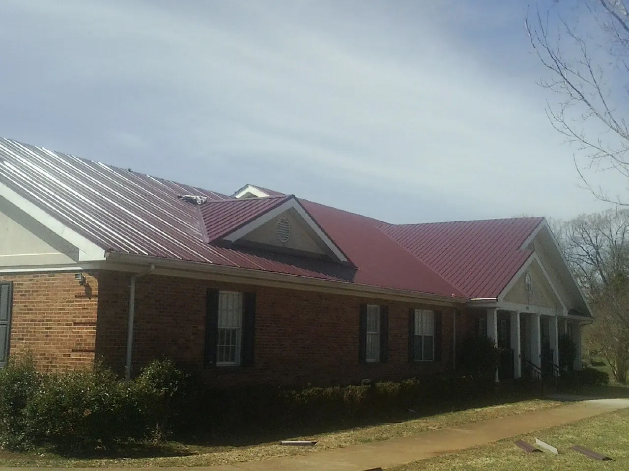 Red metal roof with gabled entries on a long brick building, from a Hail Damage Roof Repair job in Beaver Dams