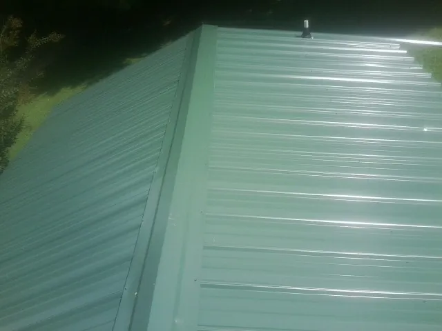 New green metal panels meeting at the ridge of a roof — Flat Roof Repair work by our crew in Beaver Dams