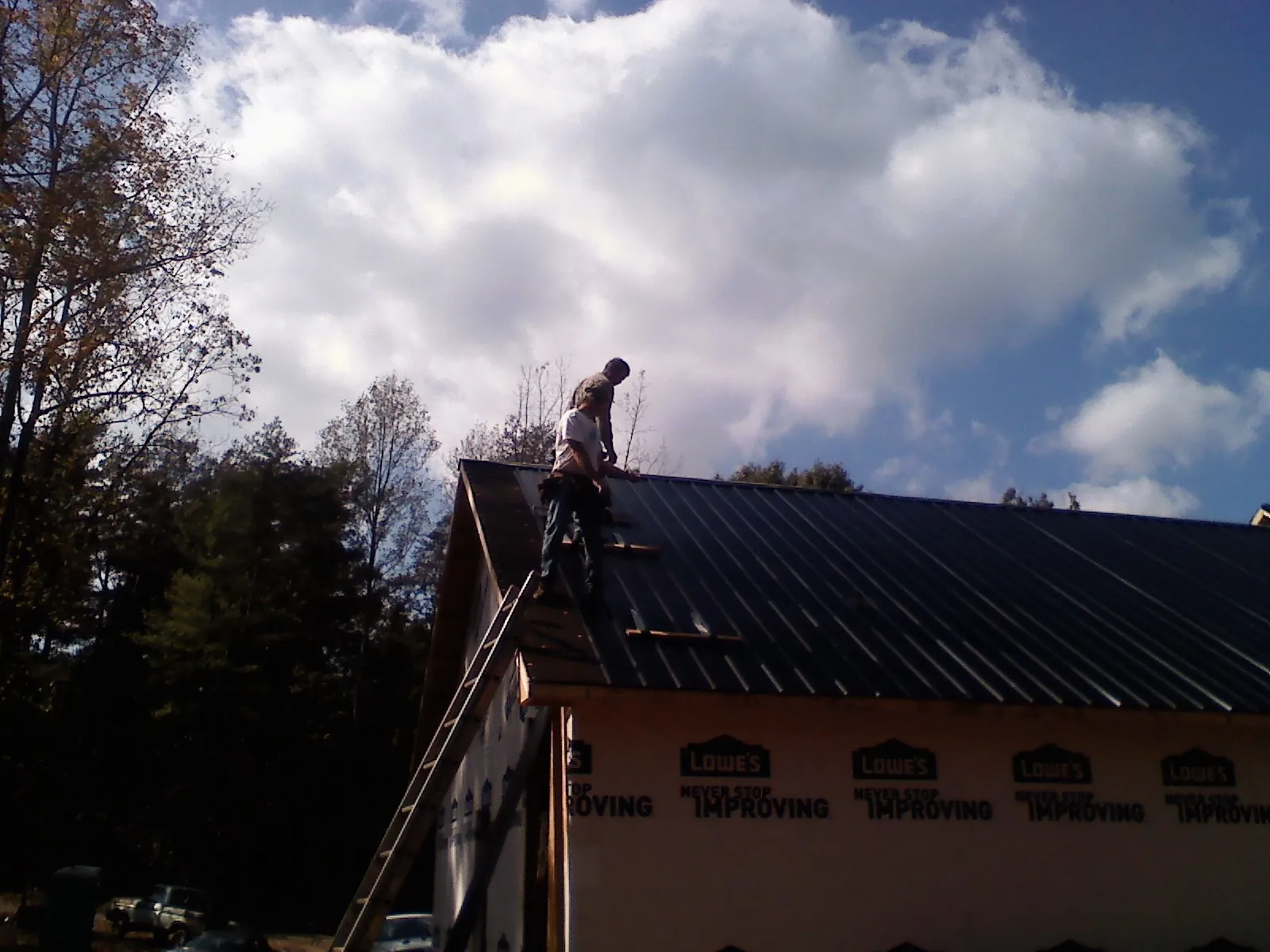 Roofer fastening dark metal panels high against a cloudy sky, from a Roof Inspection job in Beaver Dams