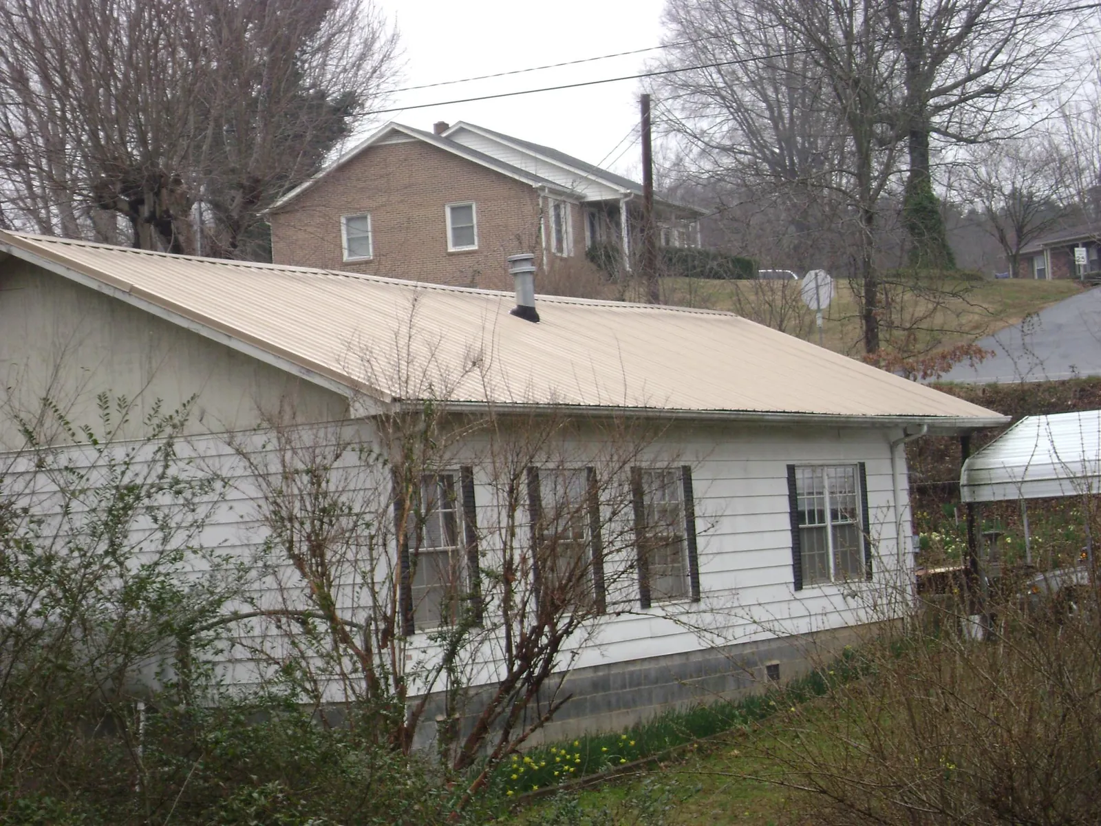 Tan metal roof on a white sided house set into a hillside — Commercial Roofing by Roofing Brothers in Beaver Dams