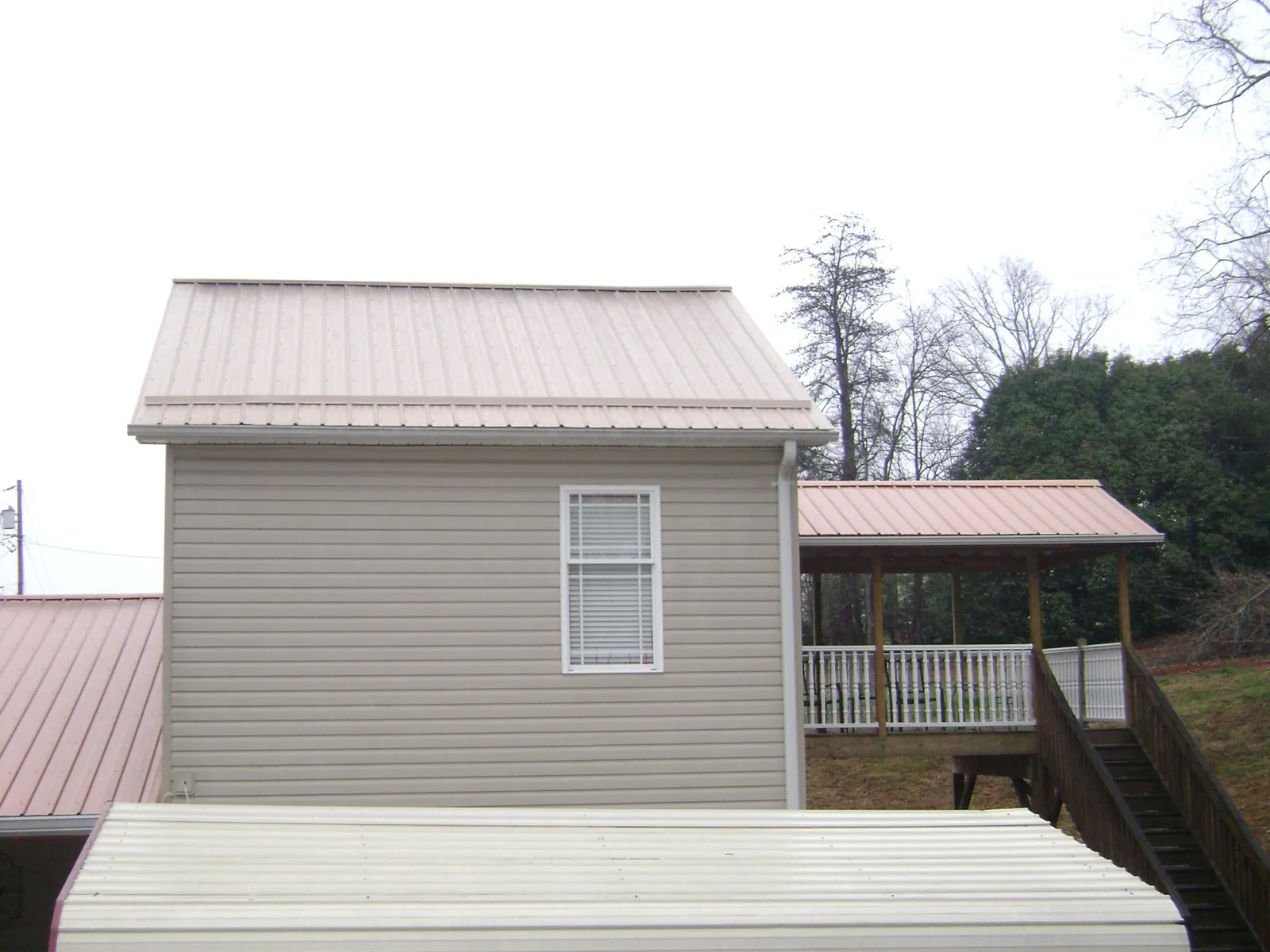 Tan metal roofs on a two story addition and attached porch, from a Roof Replacement job in Beaver Dams