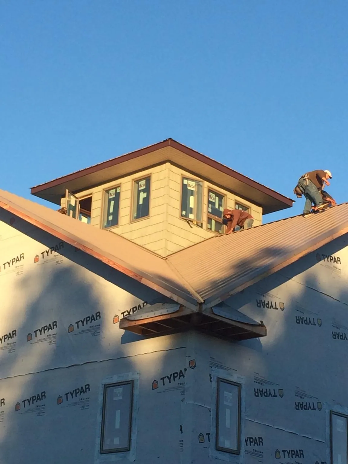 Roofers working around a rooftop cupola on a new metal roof at sunset — Roof Waterproofing in Beaver Dams by Roofing Brothers